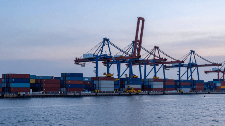 Contenedores apilados y grúa pórtico en una terminal portuaria al amanecer